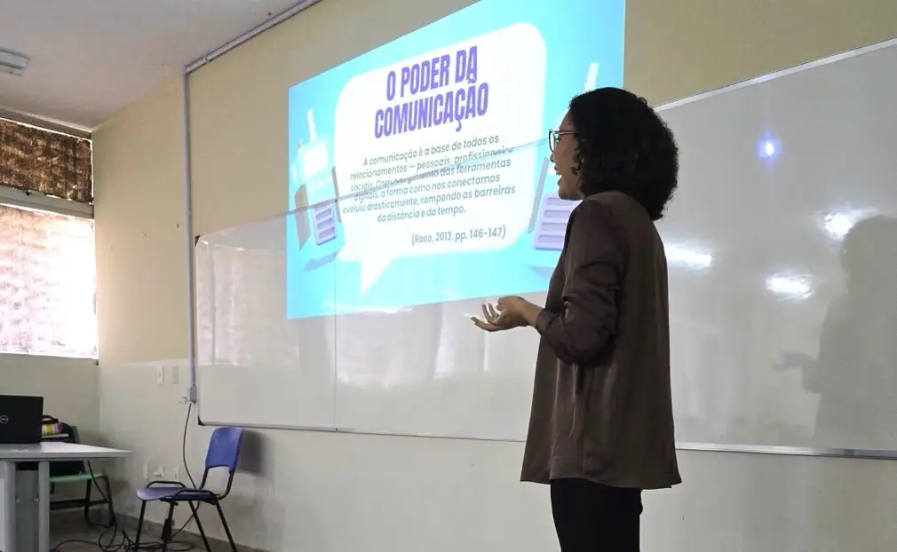 Margella dando aula, com o slide “O poder da comunicação” ao fundo.