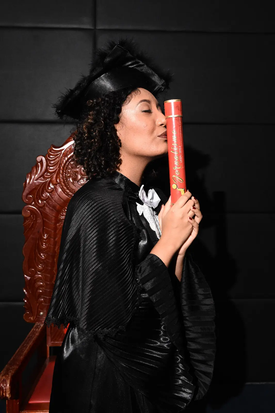 Margella na formatura, de beca, beijando o canudo.